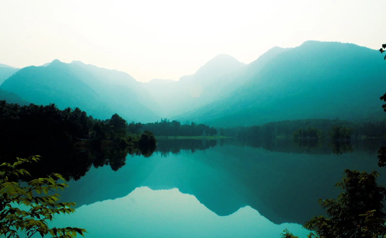 Misty green mountains reflected in the still waters of the Kozhikode region